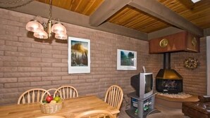 A cozy room with a brick wall, wooden ceiling, a fireplace, a television, and a dining table with chairs.