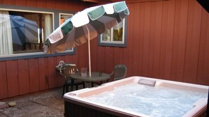 Un jacuzzi con terraza de madera, una mesa con sillas y una ventana con vista a la casa.