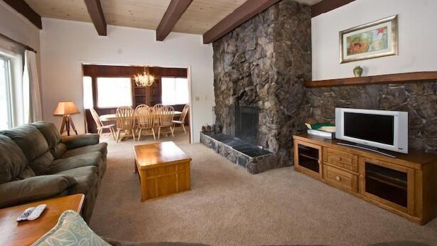 Una sala de estar acogedora con chimenea de piedra, un televisor sobre un mueble de madera, un sofá y un comedor con sillas.