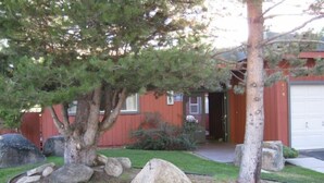 Propiedad residencial con garaje rojo, entrada para vehículos y césped con rocas grandes y un árbol.