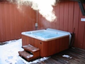 A hot tub in a backyard with a wooden deck and steps leading up to it.