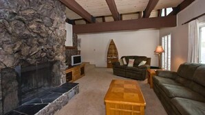 Una sala de estar con chimenea de piedra, vigas de madera, un sofá, una mesa de centro y una estantería.