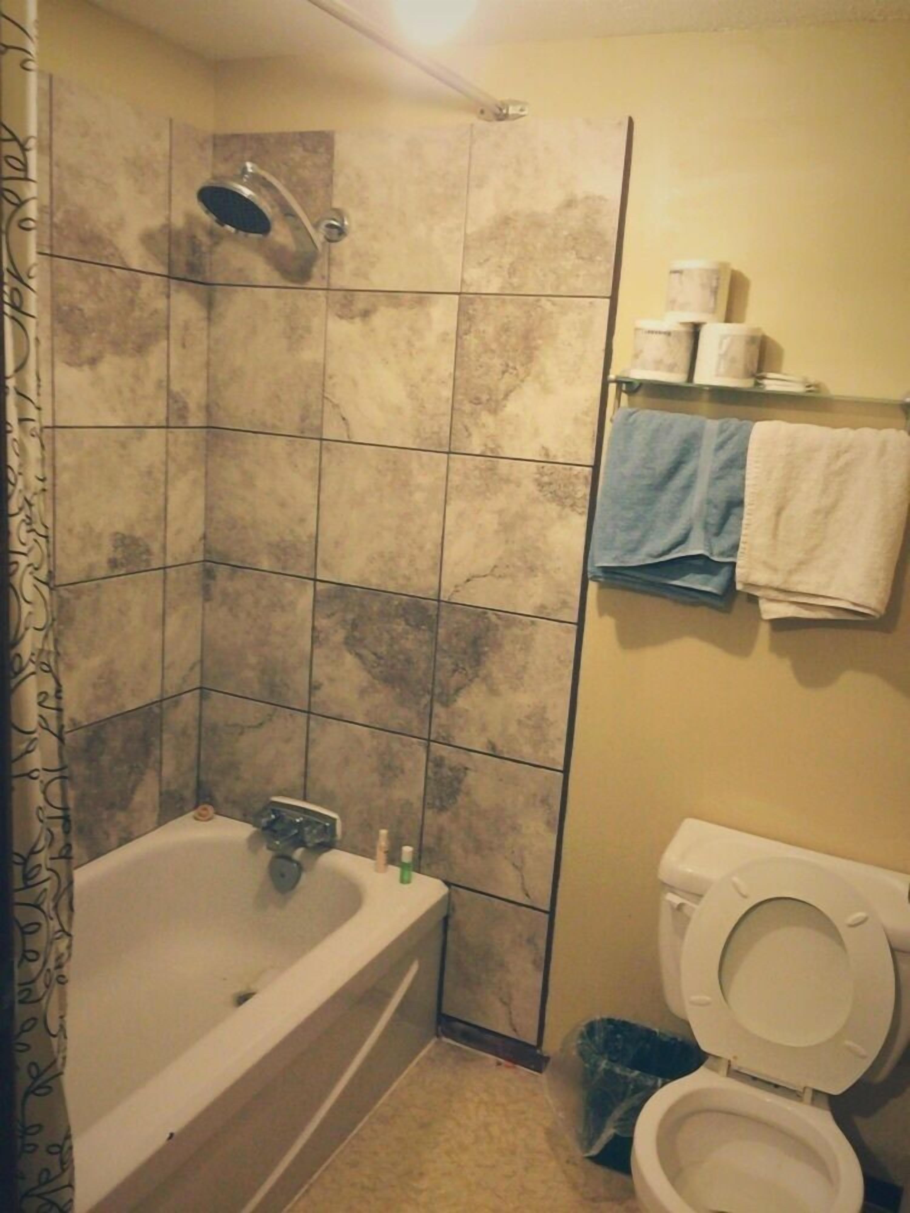 A bathroom with a bathtub, a shower, a toilet, and a shelf with towels.