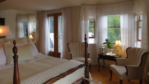 A bedroom with a large bed, two chairs, a small table with a lamp, and a window with curtains. - Atlantic Ark Inn (Boothbay Harbor)