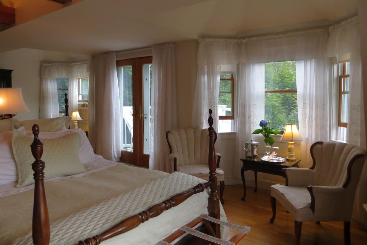 A bedroom with a large bed, two chairs, a small table with a lamp, and a window with curtains.
