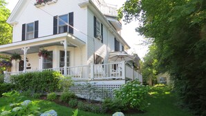 A two-story house with a porch, surrounded by lush greenery and hydrangea flowers. - Atlantic Ark Inn (Boothbay Harbor)