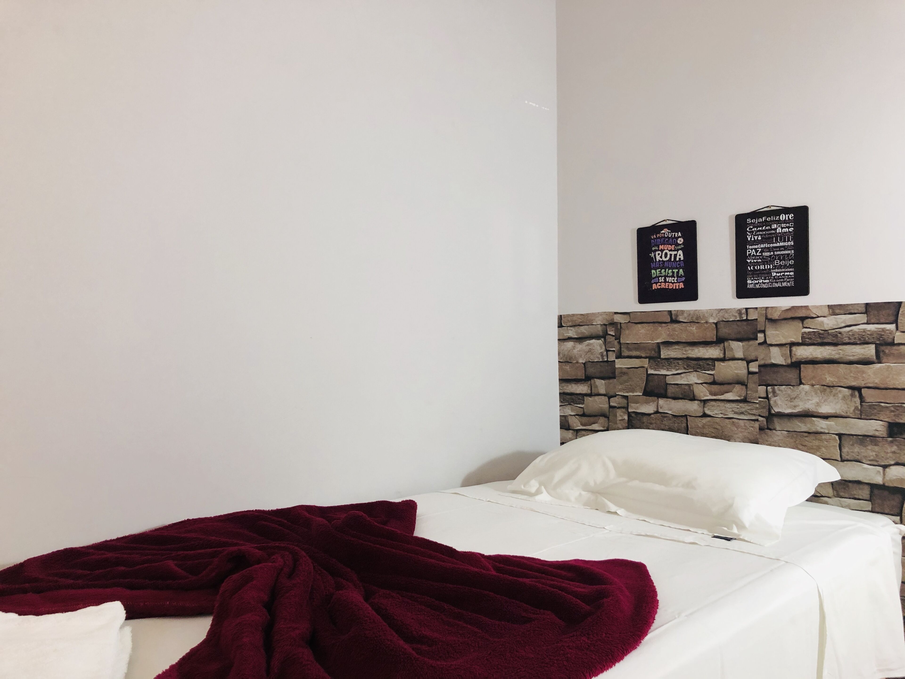 A bedroom with a stone headboard, white bedding, and a red blanket.