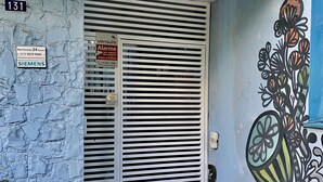 A building entrance with a metal gate, a number sign '131', and a wall with a floral mural. - Kera Smart Hostel (São Paulo)