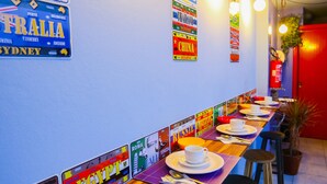 A long dining table with multiple chairs, a red door, and wall decorations with country names. - Kera Smart Hostel (São Paulo)