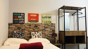 A neatly made bed with a red pillow, a stone wall behind it, and motivational signs on the wall. - Kera Smart Hostel (São Paulo)