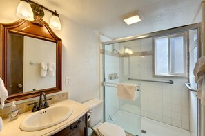 A bathroom with a large mirror, a sink, a toilet, and a glass-enclosed shower.