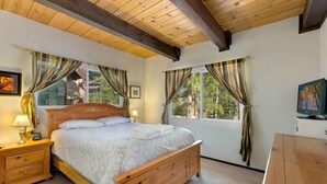 Un dormitorio con una cama de madera, dos mesitas de noche, un escritorio de madera y una ventana con cortinas.