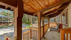 Una terraza de madera con una silla mecedora, barandas de madera y vistas a una carretera y árboles.