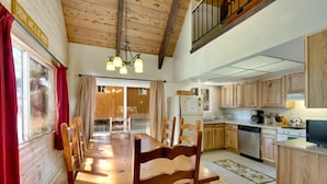 Un interior de madera con una mesa de comedor, sillas, una cocina con armarios de madera y una escalera.