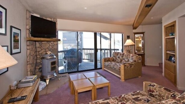 A cozy living room with a stone fireplace, a flat-screen TV, a sofa, and a coffee table.