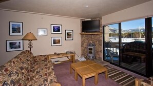 A living room with a sofa, a coffee table, a stone fireplace, a television, and framed pictures on the wall.