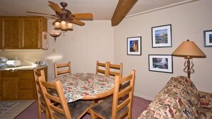 A dining area with a round table, chairs, a ceiling fan, wooden cabinets, and framed pictures on the wall.