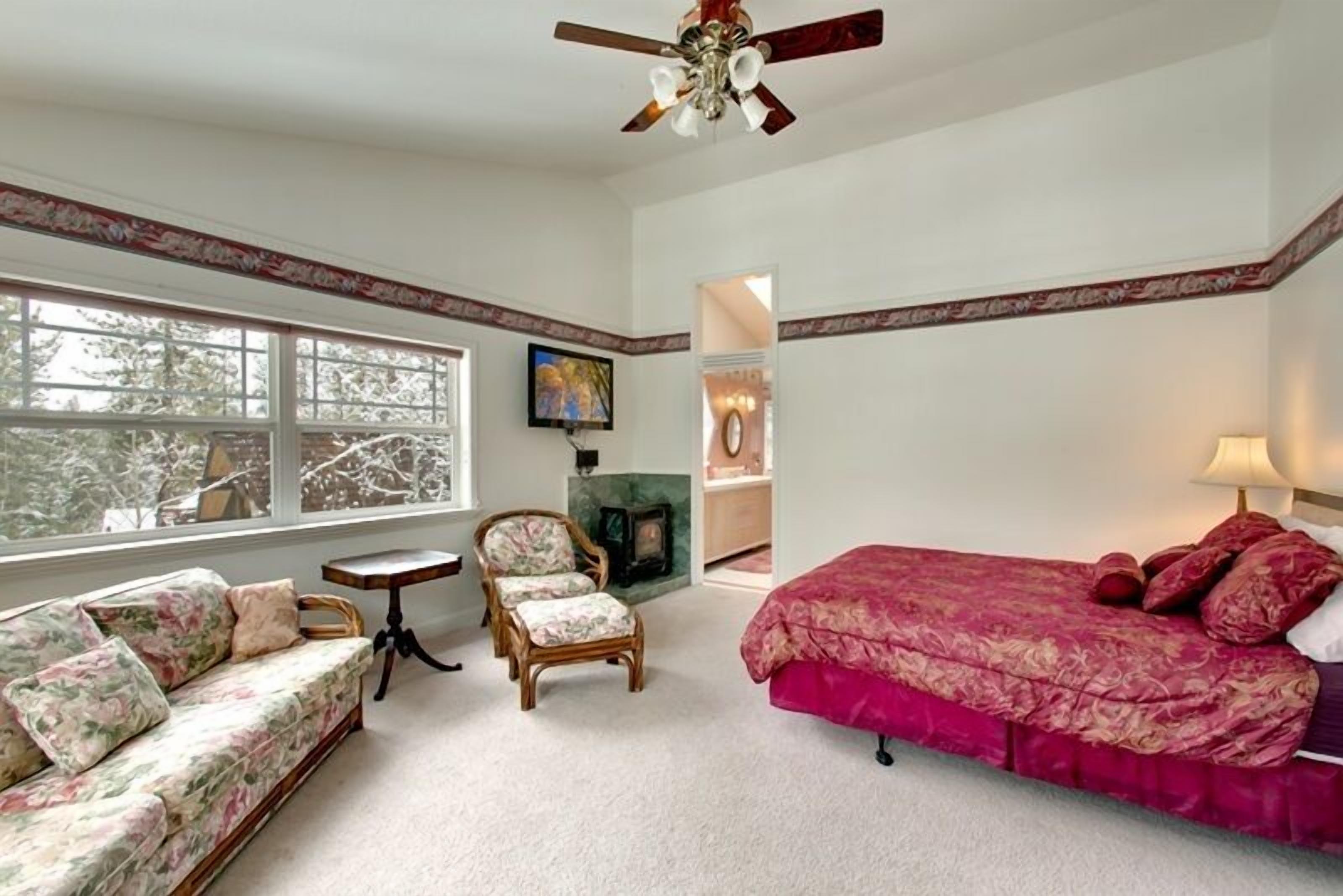 A bedroom with a large window, a bed, a sofa, a chair, and a small table.