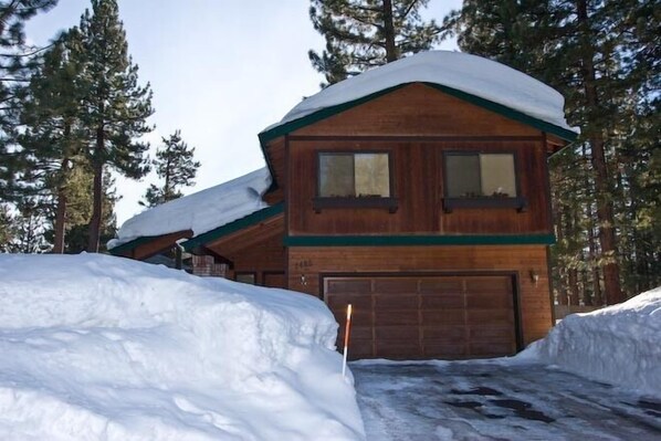 A wooden cabin with a garage, surrounded by snow and trees. - 2485 Tepee Ct. (South Lake Tahoe)