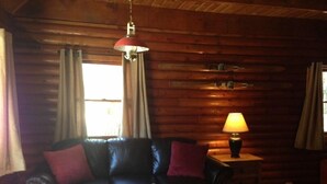 A cozy log cabin interior with a leather sofa, a small table with a lamp, and a hanging light fixture.