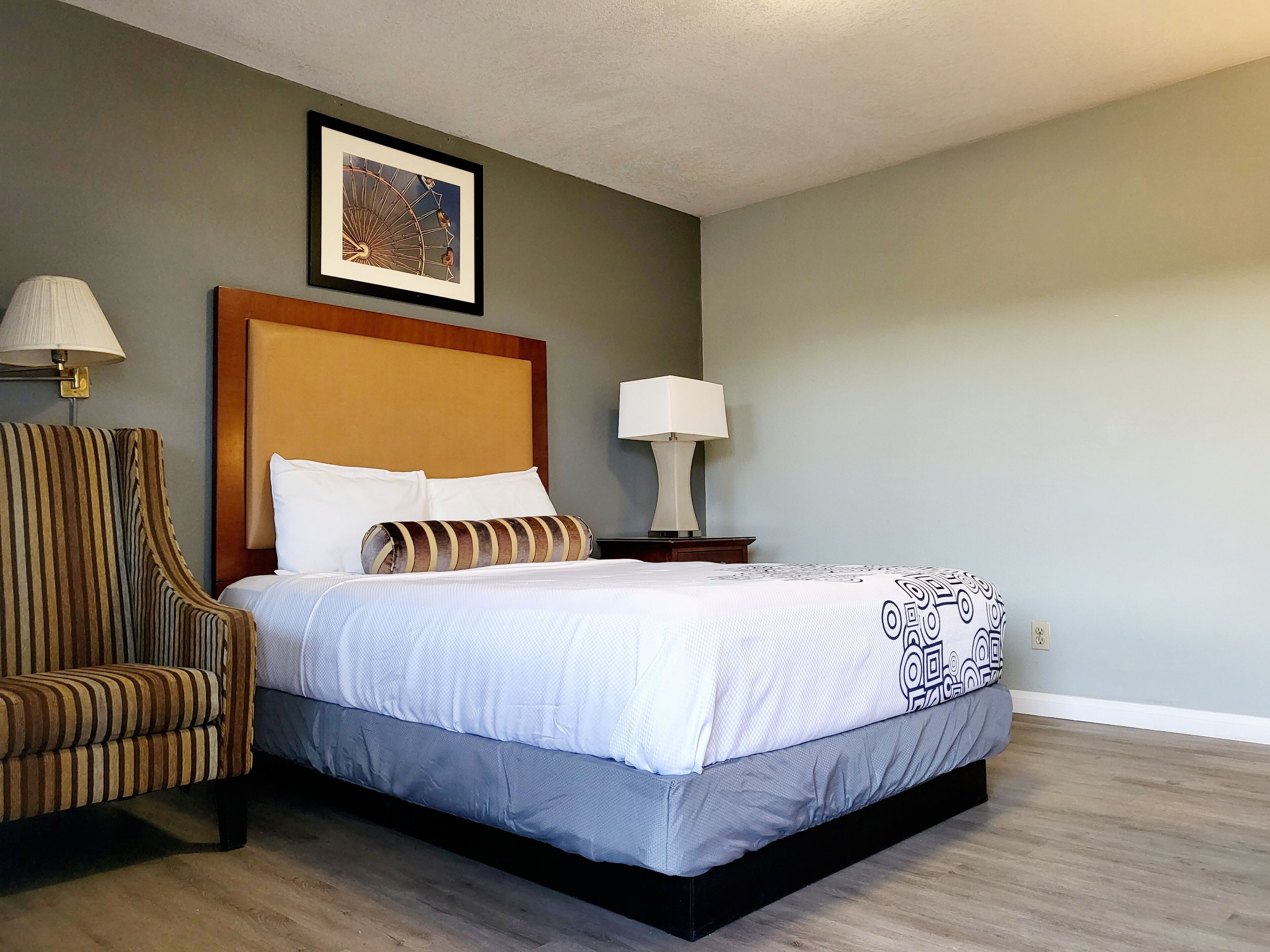 A hotel room with a bed, a striped armchair, two bedside lamps, and a framed picture on the wall.