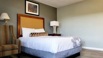 A hotel room with a bed, a striped armchair, two bedside lamps, and a framed picture on the wall.