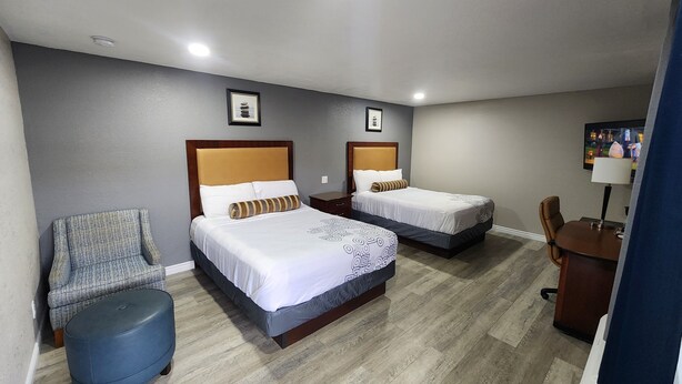 A hotel room with two beds, a chair, a desk, and a TV. - Star Inn (Barstow)