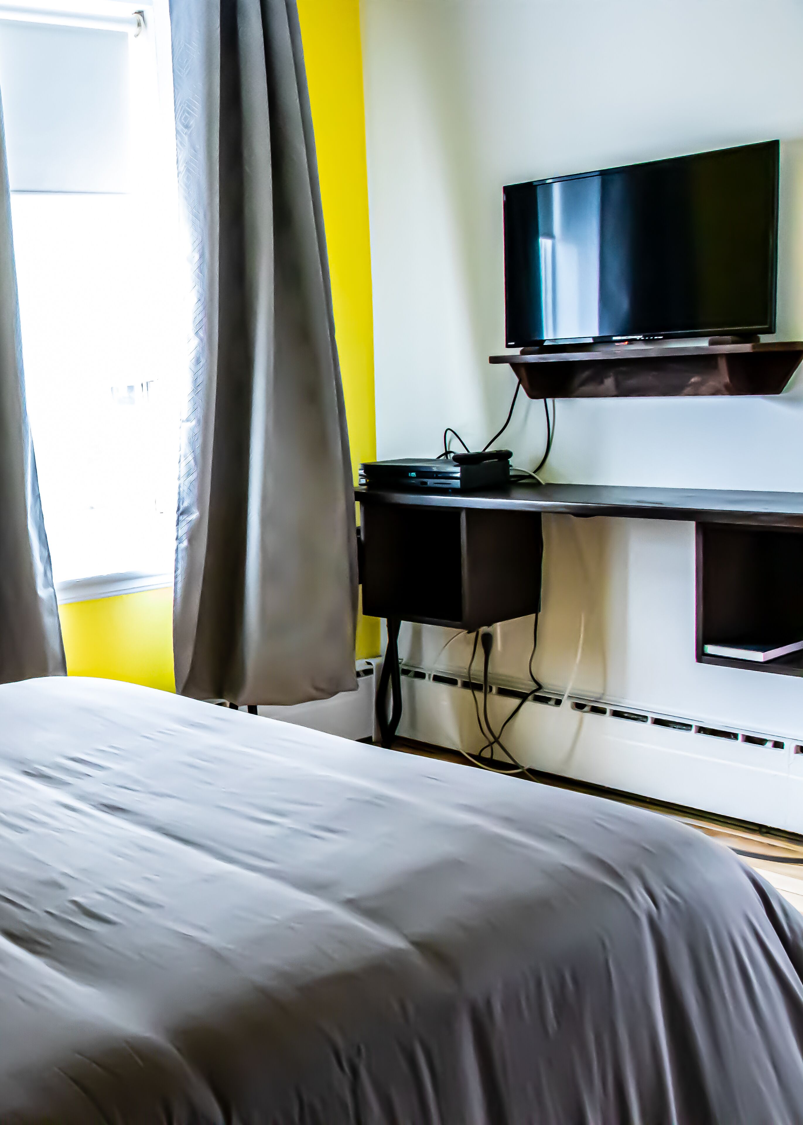 Habitación de hotel con cama, televisor sobre un mueble bajo y escritorio con computadora.