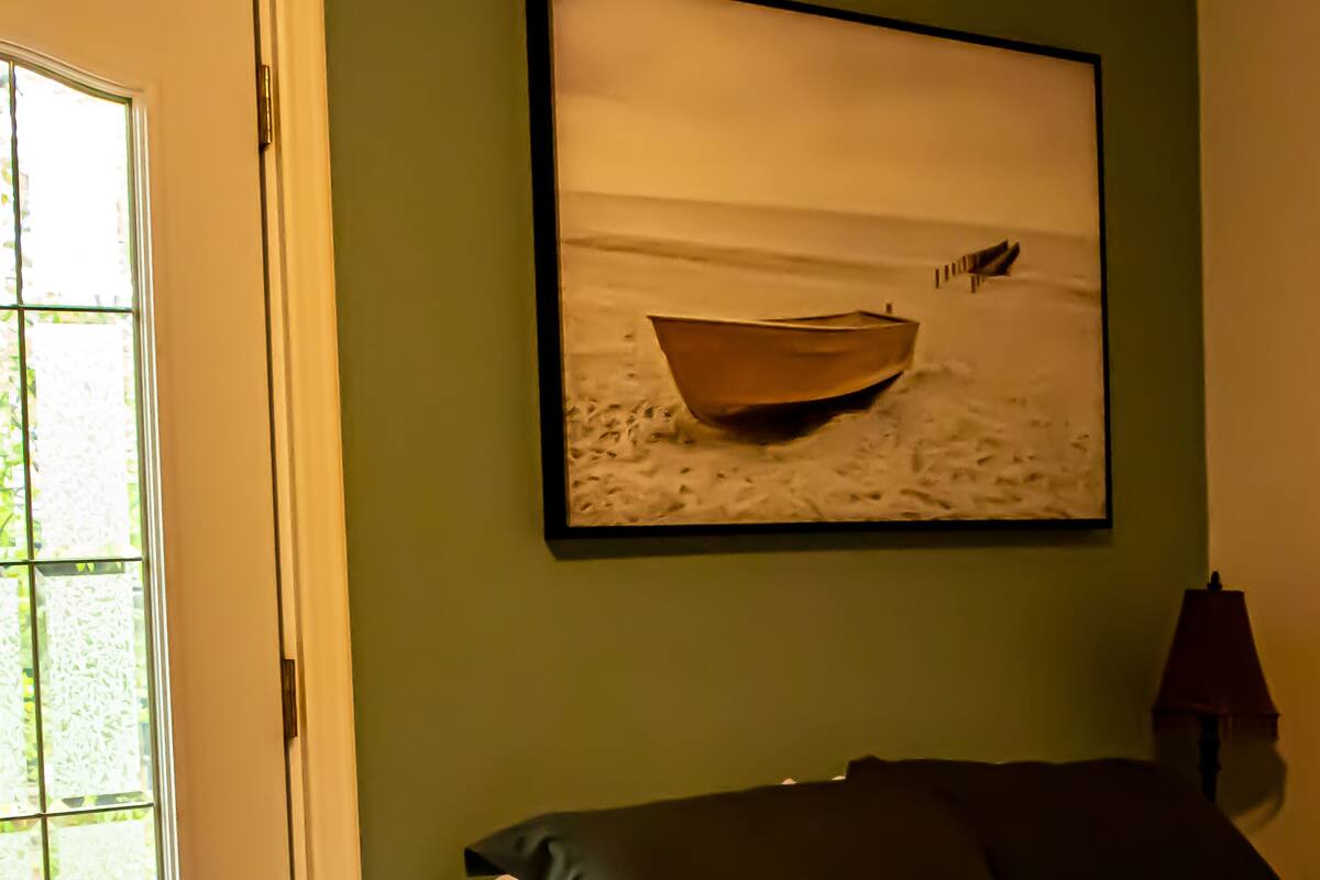 Un dormitorio con una cama, una ventana que ofrece vistas a una playa y un cuadro de un barco en la pared.
