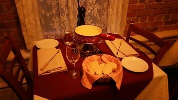 Una mesa de comedor dispuesta con platos, cubiertos, una copa de vino, una cesta de pan y una botella.