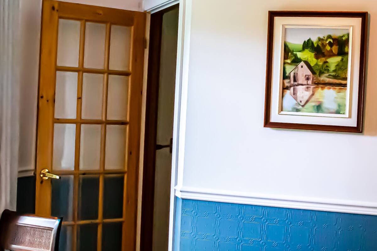 Un dormitorio con cama, una silla, una puerta y un cuadro enmarcado en la pared.