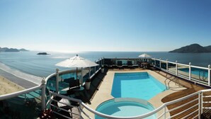 Et poolområde med havudsigt, en strand og en lounge med parasoller.