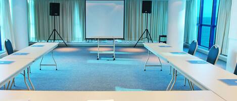 A conference room with a long table, chairs, a projector, and a whiteboard.