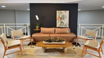 Uma sala de estar moderna com um sofá, duas poltronas, uma mesa de centro com flores, uma planta em vaso e uma parede com uma impressão botânica.