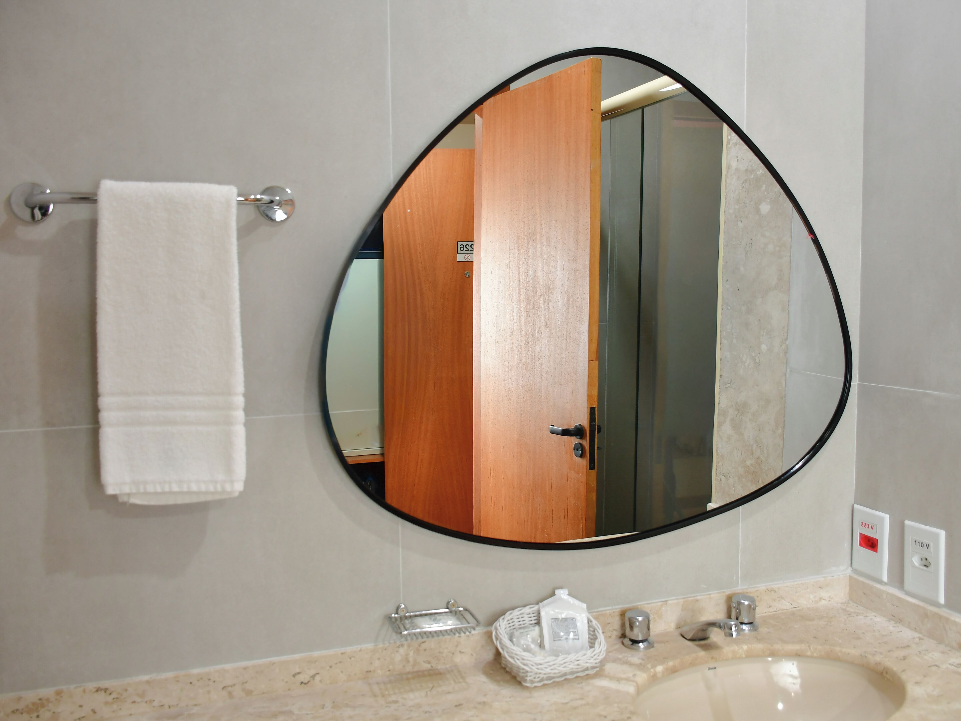 Un baño con un espejo redondo, un perchero, un lavabo y una puerta de madera.
