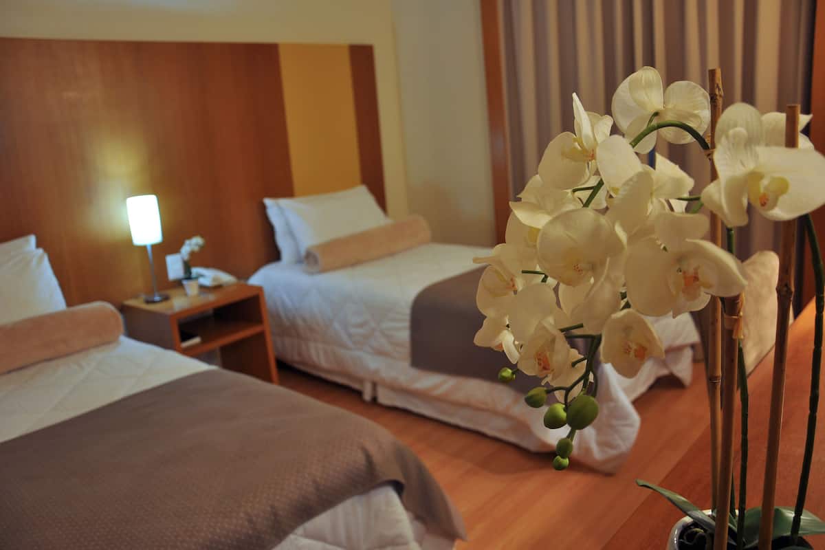 A hotel room with two beds, a nightstand, a lamp, and a potted orchid plant.