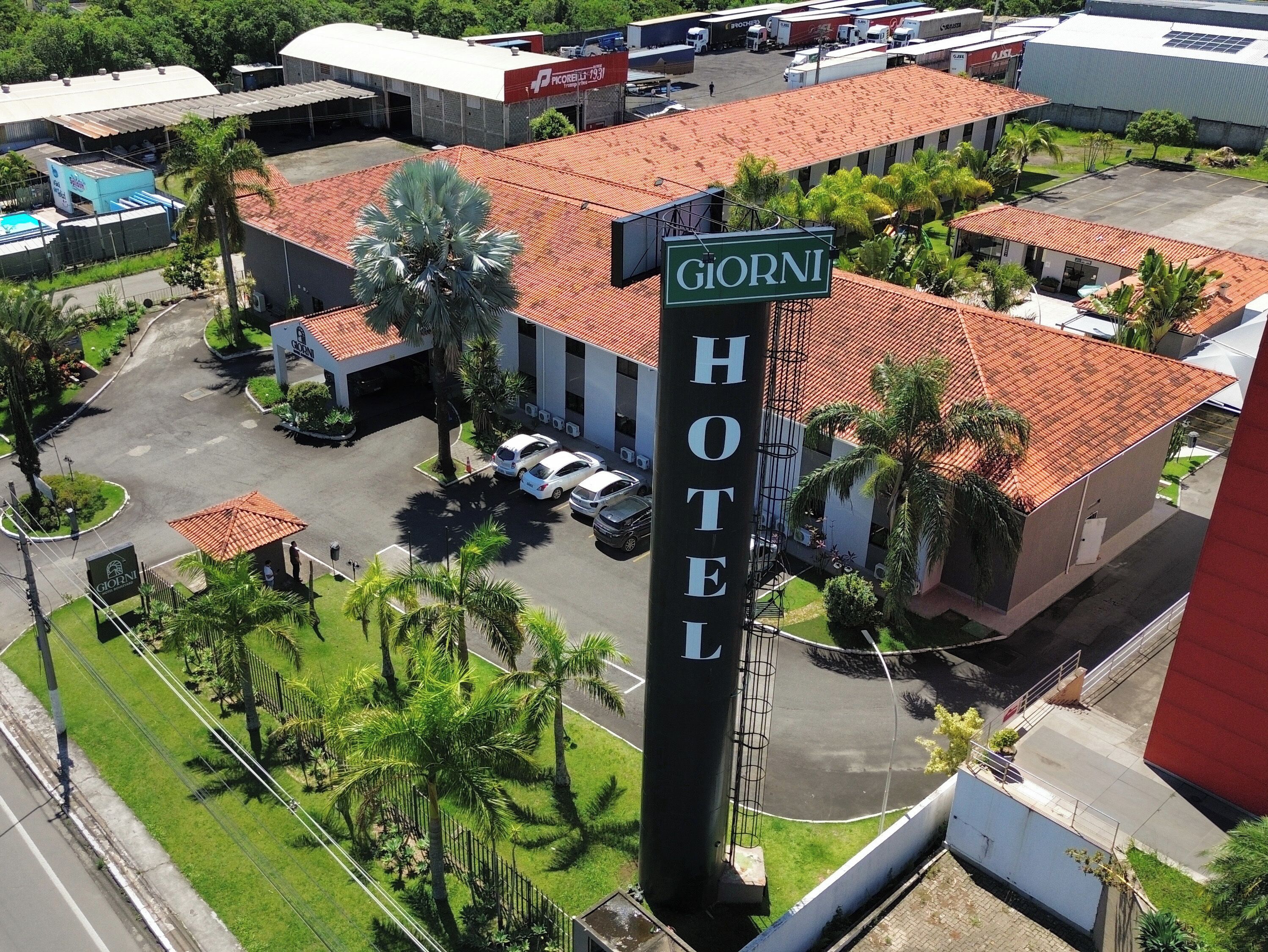 Un hotel chiamato 'Giorni' con un tetto in tegole rosse, un parcheggio e vegetazione circostante.