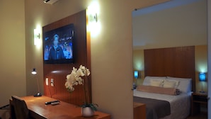 A hotel room with a TV mounted on the wall, a desk with a lamp, a chair, and a bed with a headboard. -  Giorni Hotel Boulevard (Resende)