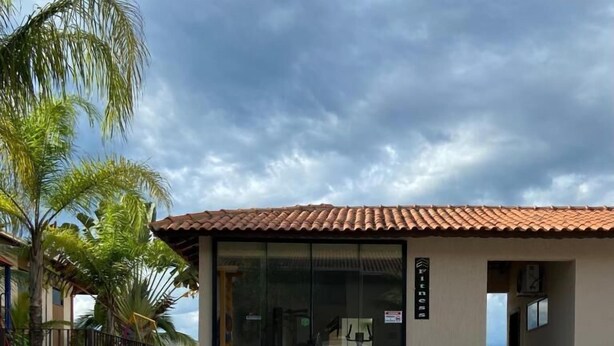 A swimming pool with a tiled deck, a building with a tiled roof, and palm trees. -  Giorni Hotel Boulevard (Resende)