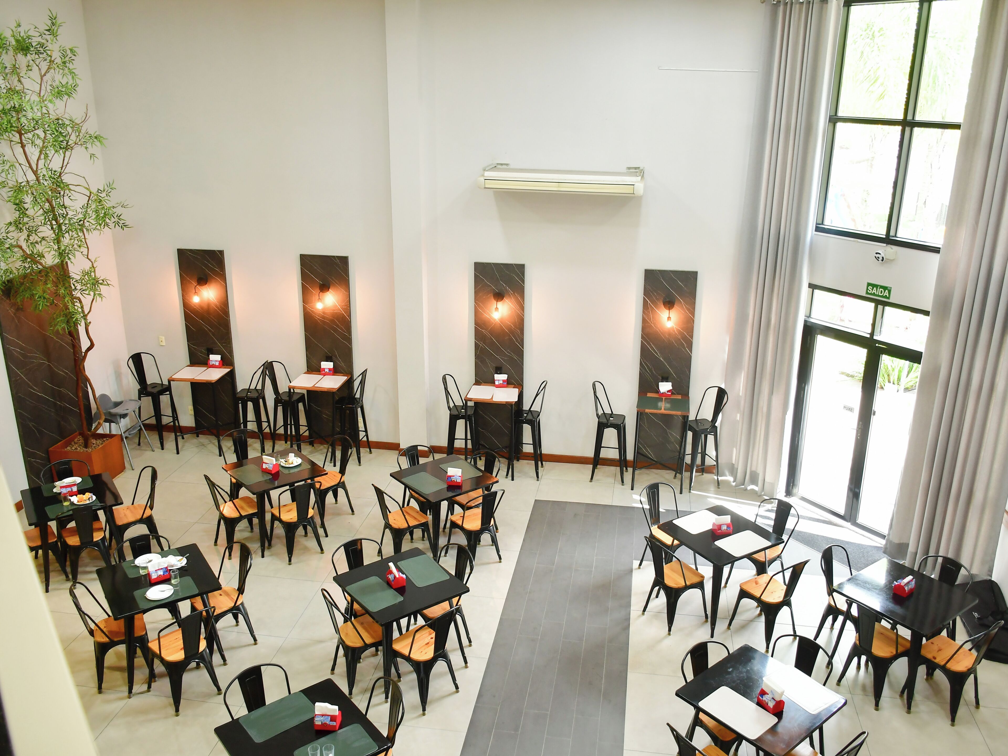 Un restaurante con varias mesas y sillas, una planta en maceta y un letrero que indica la salida.