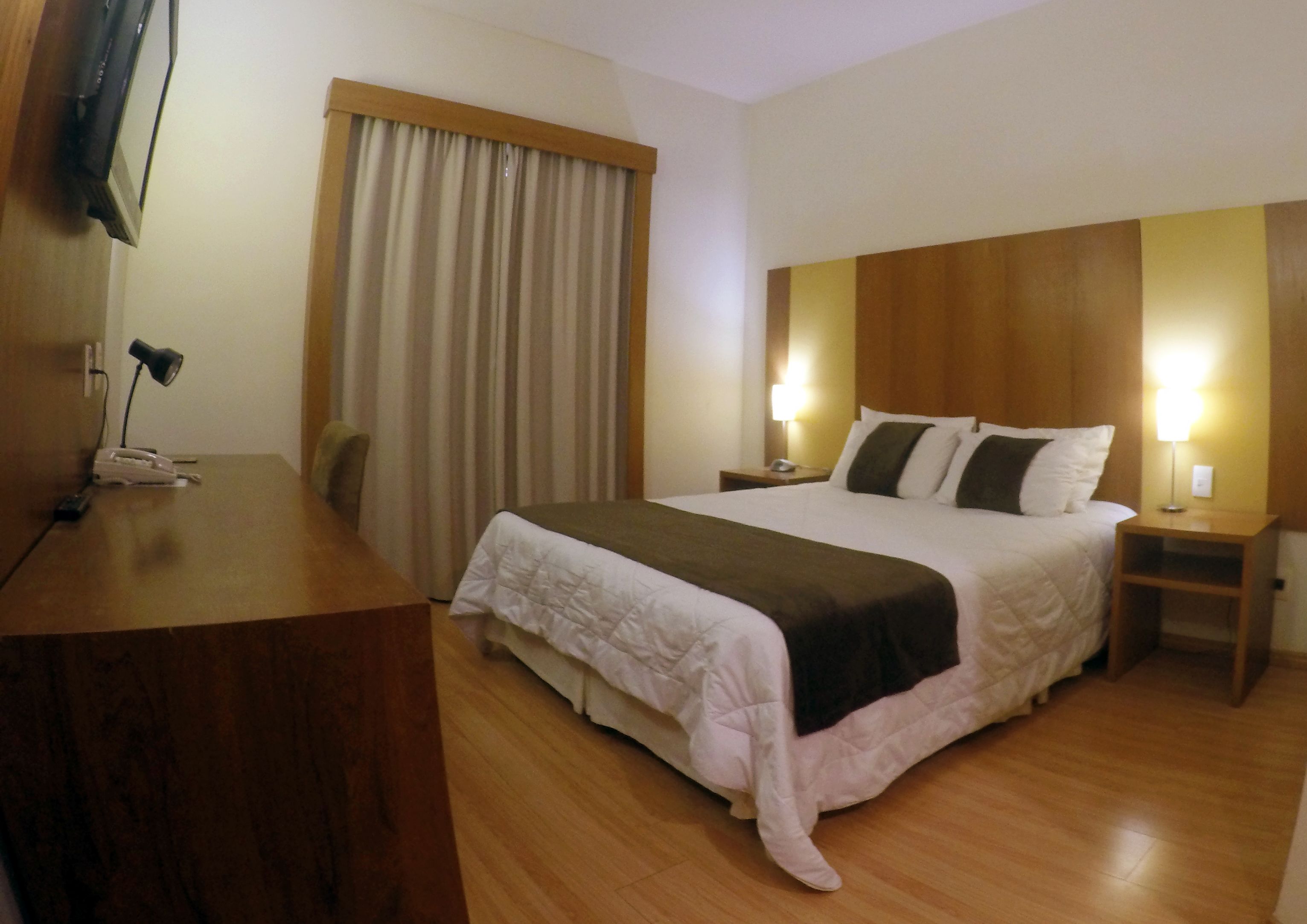 A hotel room with a wooden bed, a desk with a telephone, and a television on the wall.
