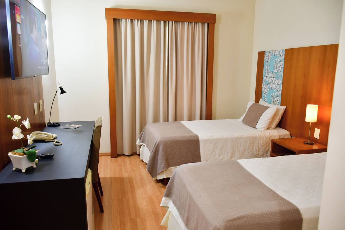 A hotel room with two beds, a desk with a telephone, a TV, and a lamp.