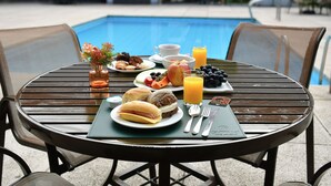 A dining table with breakfast items, a glass of orange juice, and a view of a swimming pool. -  Giorni Hotel Boulevard (Resende)