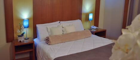 Une chambre d’hôtel avec un grand lit, deux tables de chevet, une petite table et une lampe fixée au mur.