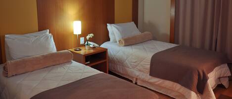 A hotel room with two beds, a nightstand with a lamp, and a window with curtains.