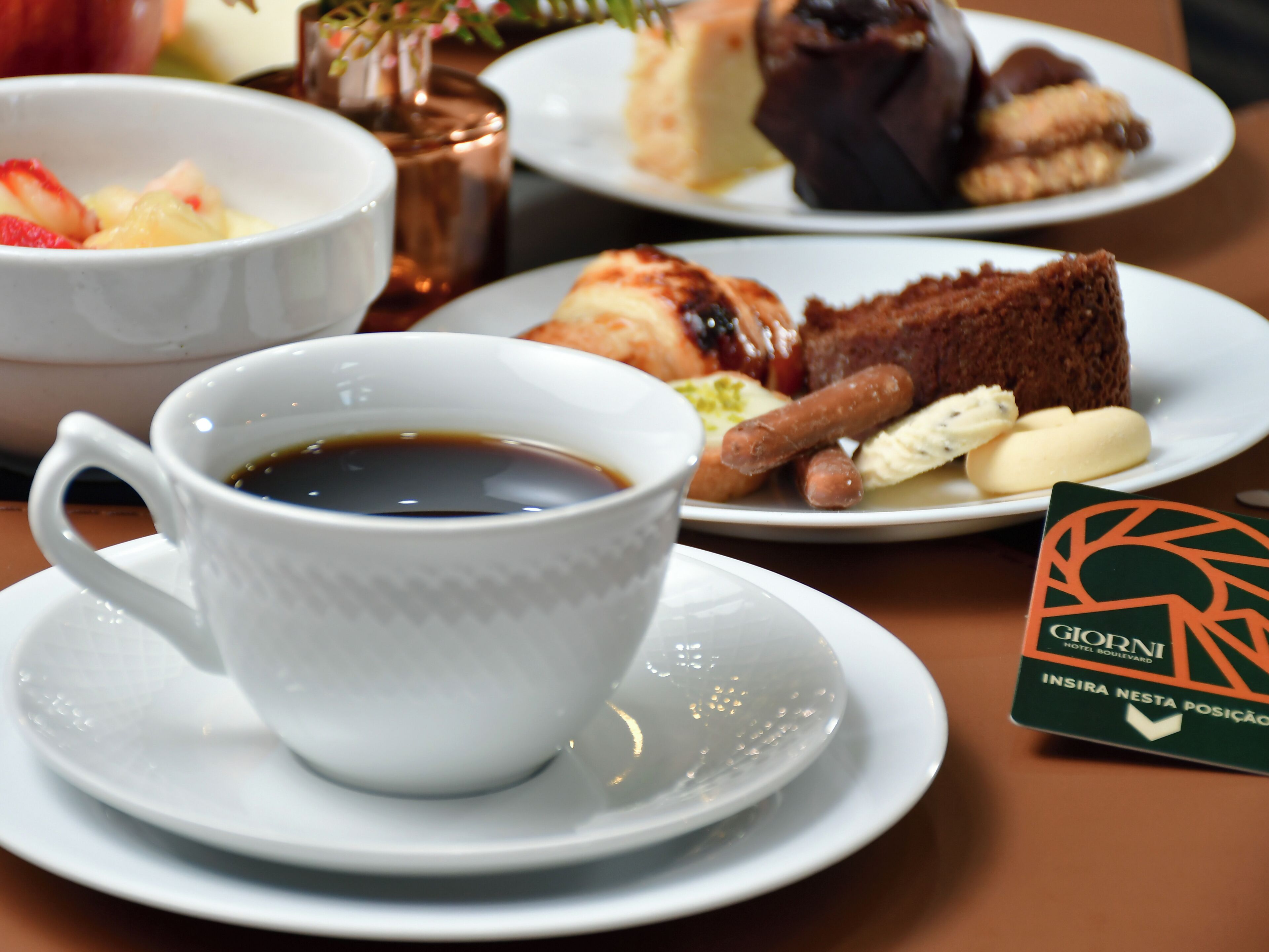 Una mesa con una taza de café, un plato con una porción de pastel y un plato con pastelería.