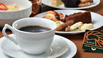 Una mesa con una taza de café, un plato con una porción de pastel y un plato con pastelería.