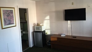 A compact hotel room with a kitchenette, a flat-screen TV mounted on the wall, a wooden dresser, and a framed picture on the wall. - Mayo Inn (Roswell)