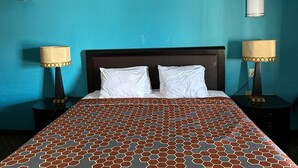 A hotel room with a blue wall, a wooden headboard, two white pillows, a patterned bedspread, and two bedside lamps. - Mayo Inn (Roswell)