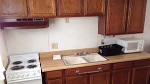 A kitchen with wooden cabinets, a white stove, a double sink, and a microwave. - Mayo Inn (Roswell)